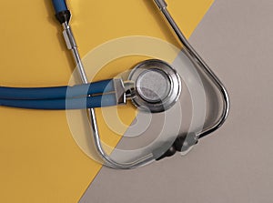 Medical tool, blue stethoscope on gray and yellow background, top view