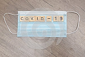 Wooden letters and numbers add up to the word: covid 19. Items are laid out on a protective mask