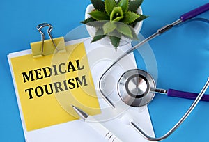 MEDICAL TOURISM - words on a yellow notebook on a blue background with a stethoscope and a cactus