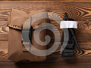 Medical tourniquet to stop the blood and a military first aid kit on a brown textured wood.