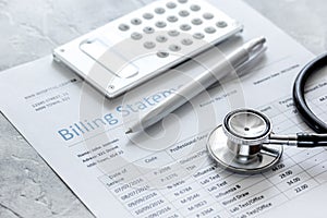 Medical treatmant billing statement with stethoscope and calculator on stone background