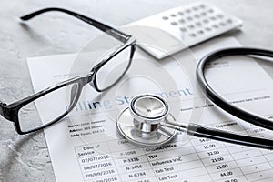 Medical treatmant billing statement with stethoscope and glasses on stone background