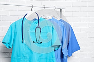 Medical uniforms and stethoscope hanging on rack near white brick wall