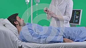 Adult man patient laying in bed with drip and monitor, female nurse draws injection in syringe holding in hand. Isolated