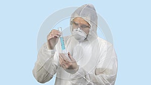 Medical worker in antiviral protective clothing holding test tube with blue liquid.