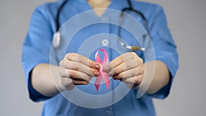 Medical worker in blue uniform holding pink ribbon in hands, breast cancer risk