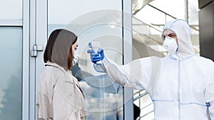 Medical worker in hazmat suit measuring temperature with non contact thermometer