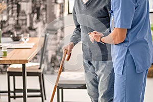 Medical worker helping his patient to walk with a cane
