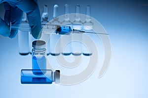 Medical worker holds an ampoule with vaccine and medical disposable syringe in his hand. Blue background.