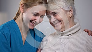 Medical worker hugging and supporting smiling elderly lady in nursing home