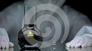 Medical worker looking at ampule with antidote on table near poison in flask photo