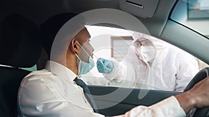 Medical worker in personal protective equipment swabbing a person in a car drive through