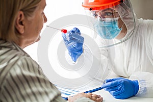 Medical worker in personal protective equipment wearing face shield performing PCR COVID-19 nasal swab test