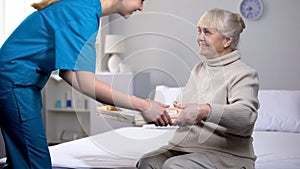 Medical worker serving dinner to old female patient, taking care of granny