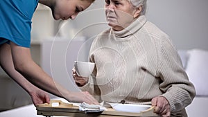 Medical worker serving dinner tray to sick elderly woman in medical center