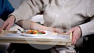 Medical worker serving tasty salad to old female patient, nursing home care