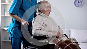 Medical worker taking care about upset senior lady in wheelchair, rehabilitation