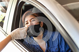 Medical worker taking nasal swab from woman in car to test for covid-19 infection.