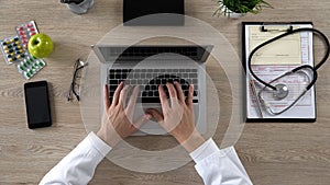 Medical worker typing on laptop, keeping electronic medical records, top view