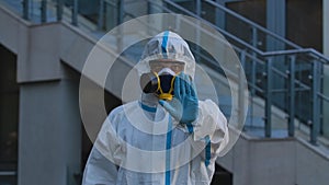A medical worker or virologist in a white protective suit and respirator showing a STOP gesture with his palm. A man
