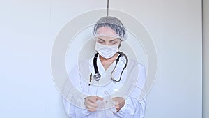 Medical worker in a white coat and a protective mask on a light background. Woman doctor video portrait. Free space for