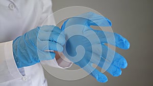 A medical worker in a white coat puts blue rubber sterile gloves on his hands. The doctor is preparing for the operation