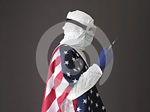 A medical worker in a white protective suit with the US flag is holding a syringe.