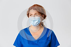 Medical workers, covid-19 pandemic, coronavirus concept. Skeptical and unamused redhead female doctor, physician looking