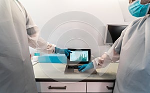 Medical workers in hazmat suit looking laptop computer for checking coronavirus cases - Doctors with protective face masks talking