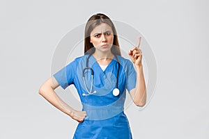 Medical workers, healthcare, covid-19 and vaccination concept. Frowning young female nurse or doctor in blue scrubs