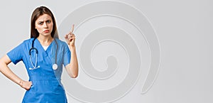 Medical workers, healthcare, covid-19 and vaccination concept. Frowning young female nurse or doctor in blue scrubs