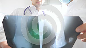 Medical workers in hospital office examine x-ray prints. Male medics consult with each other while looking at x ray