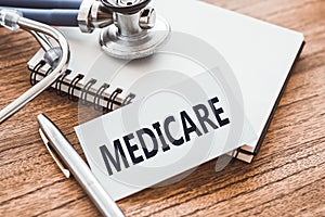 MEDICARE - text on card on wooden table with stethoscope and notepad for medical records