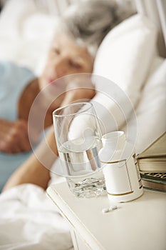 Medication On Bedside Table Of Sleeping Senior Woman