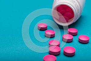 Medication bottle and bright pink pills spilled on dark blue coloured background. Medication and prescription pills.
