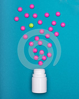 Medication bottle and bright pink pills spilled on dark blue coloured background. Medication and prescription pills flat lay.