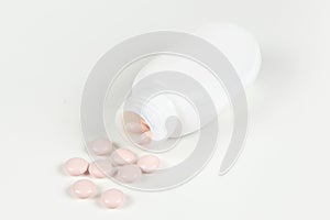 Medication bottle and white pills spilled on white background