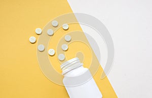 Medication bottle and white pills spilled on yellow pastel colored background. Medication and prescription pills flat lay