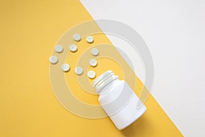 Medication bottle and white pills spilled on yellow pastel colored background. Medication and prescription pills flat lay