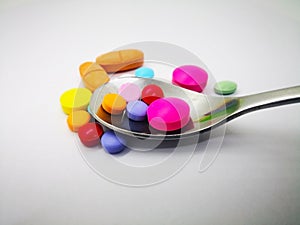 Medication and healthcare concept. Many colorful tablets of medicine, that are in silver spoon. Isolated on white