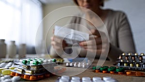 Medication lying on table, sick old woman reading prescription behind, closeup