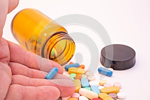 Medications in the form of pills and capsules on a white background. Hand of a man holding a blue capsule