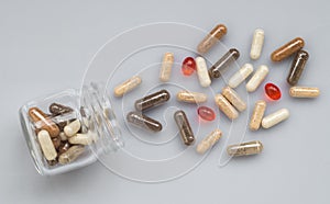 Medicinal capsule spill out of a glass jar on light surface