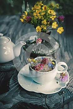 Medicinal herbal tea with chamomile flowers and a bouquet of wild flowers in a beautiful Cup on a rustic wooden background. Rustic