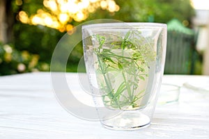 Medicinal herbal tea from Galium aparine cleavers made on wooden white table on backdrop of sunset