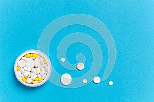 Medicine bottle with white pills and yellow capsules and dosis of different size drugs on blue background photo