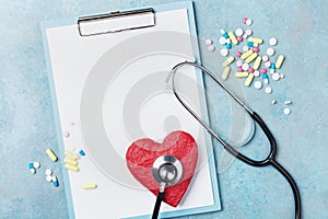 Medicine clipboard, stethoscope, drug pills, and red shape of heart on blue background top view. Healthy and cardiology concept.
