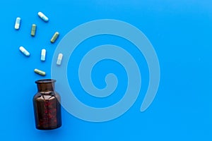 Medicine. Color capsules near pill bottle on blue background top view copy space