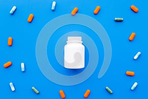 Medicine. Color capsules near pill bottle on blue background top view copy space