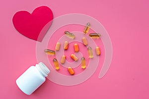 Medicine. Color capsules near pill bottle and heart sign on pink background top view copy space